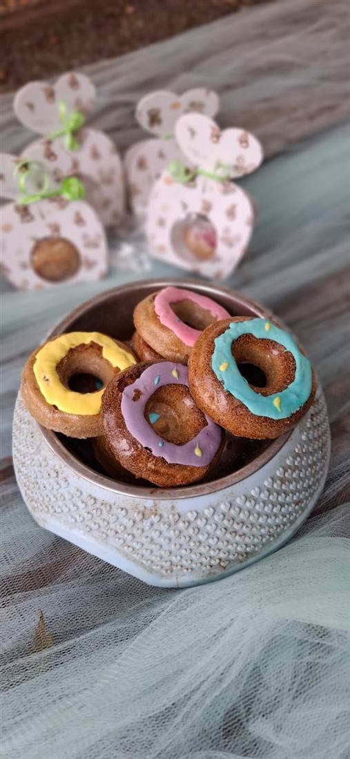 Donas para perros con glaseado amarillo, rosa, violeta y celeste en un comedero